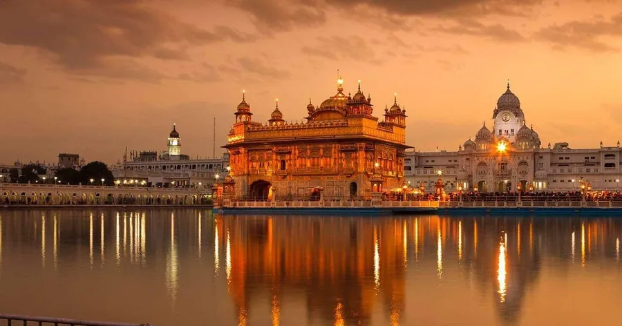 Der Goldene Tempel leuchtet in der Dämmerung orange und spiegelt sich im heiligen Becken unter einem warmen Abendhimmel